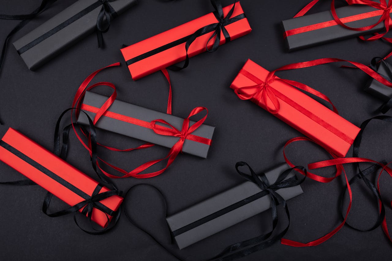 Stylish flatlay of red and black gift boxes on a black surface with decorative ribbons.